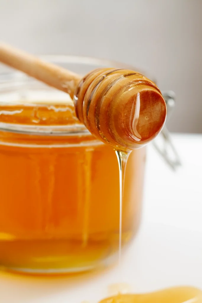 miel artesanal cayendo de una cuchara de madera, usada como remedio para la tos y endulzante natural.
